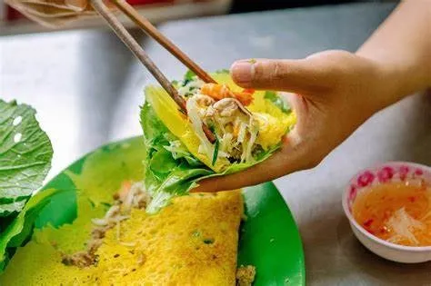 cuộn rau vào bánh xèo để ăn